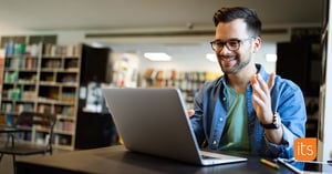 Ung mannlig lærer som ser veldig fornøyd ut mens han jobber med sin bærbare datamaskin i et klasserom eller bibliotek