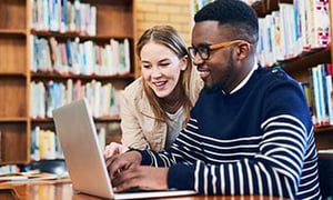 Male and female teenagers working together with a laptop in a library setting