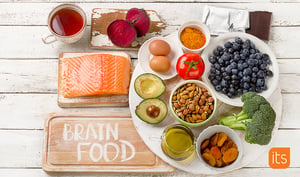 Sund hjernemad samlet på et træbord med laks, avocado, æg, nødder, blåbær, brocolli, tomat og andre sunde fødevarer.