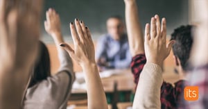 elever med händerna uppsträckta för att svara på en fråga i klassrummet