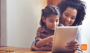 Daughter sitting on mother's lap while doing school work on a tablet.