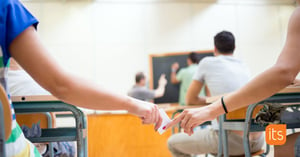 Students in a classroom passing a note from one person to another.