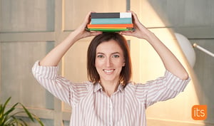 Vrouw met een goed postuur die een stapel boeken boven op haar hoofd houdt.